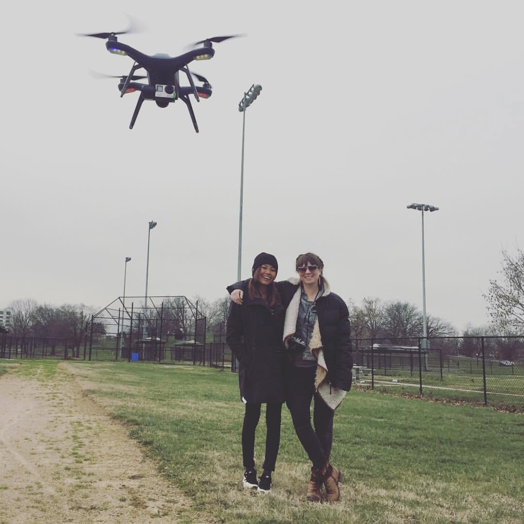 Kate and Aviator Hannah Reyes Morales stand arm in arm in a park, with a drone flying overhead.